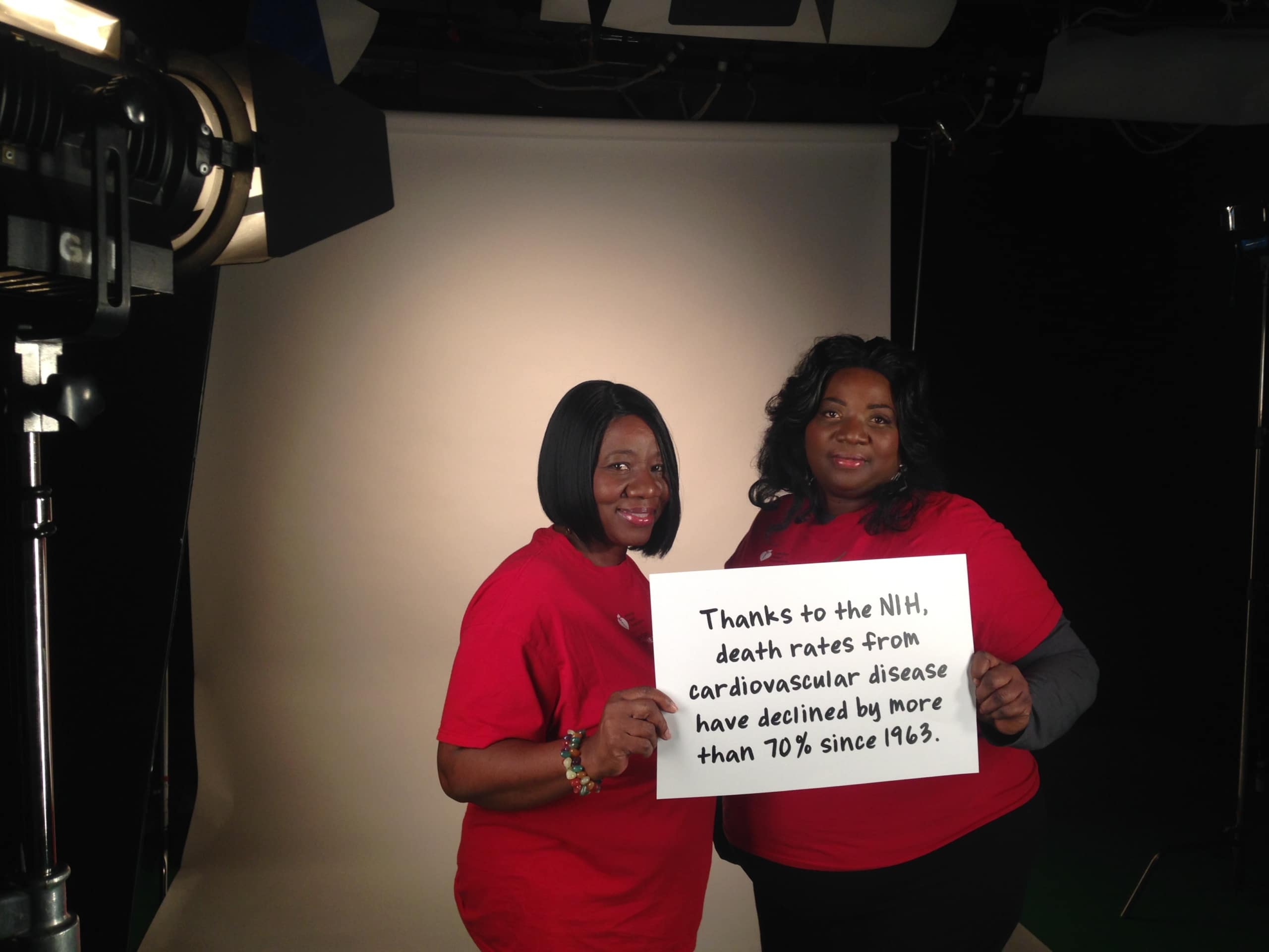 Two women holding a sign with statistics for National Institutes of Hope video shoot.