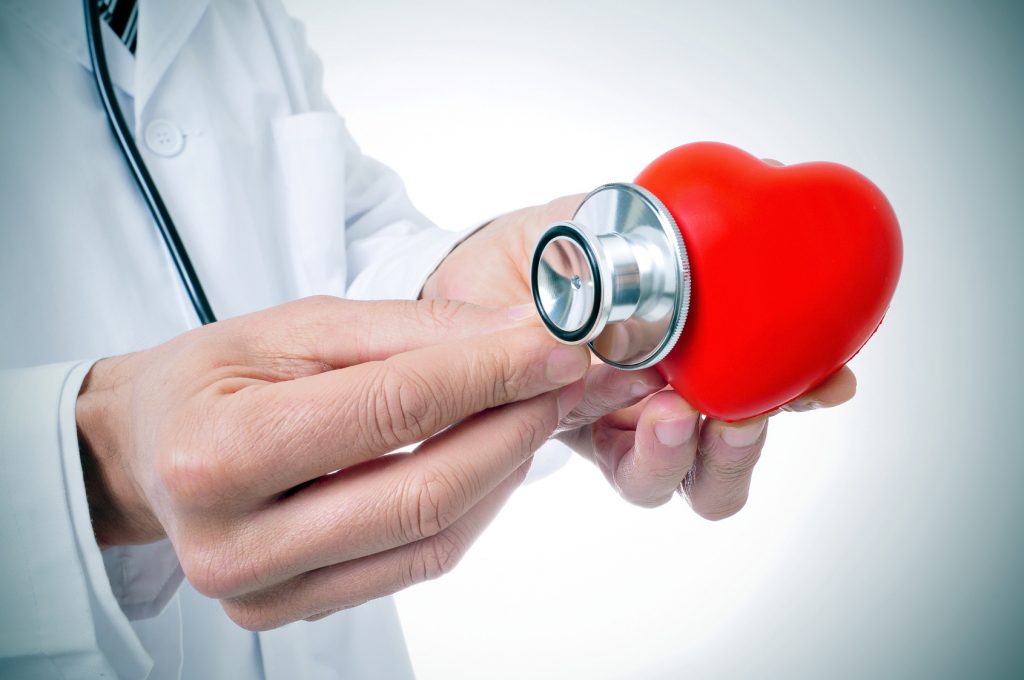 Doctor holding a stethoscope to a plastic heart.