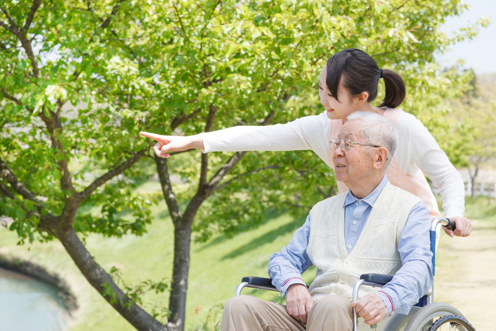 Young woman pushing elderly man in wheelchair outside.