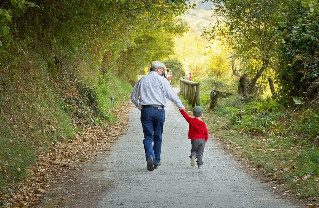 Grandfather walking down path holding hands with young boy.