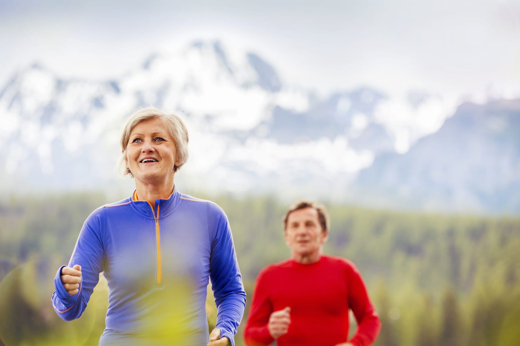 Elderly couple running outside with mountains in the background.