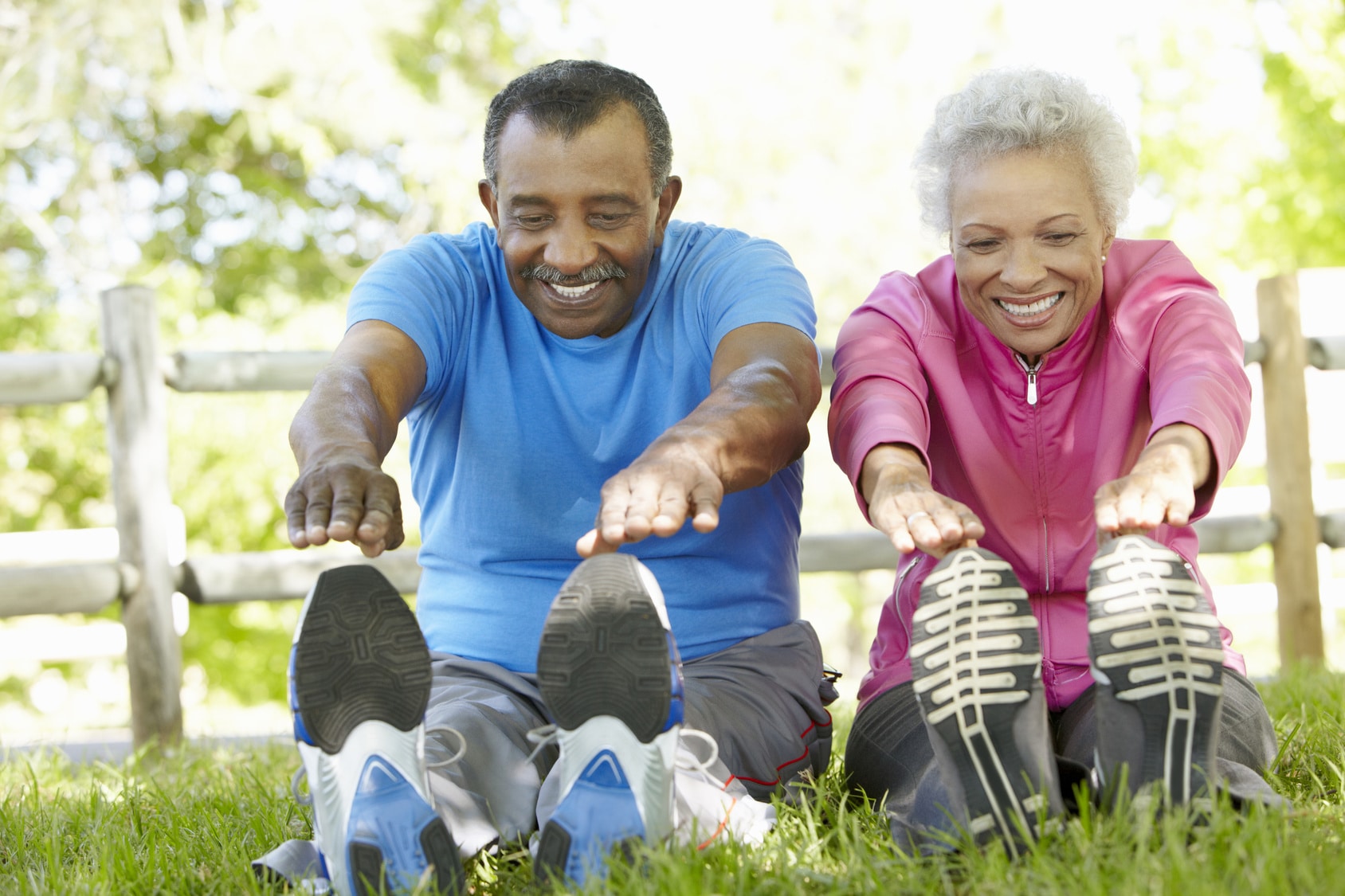 Senior couple sitting in the grass stretching to touch their toes.