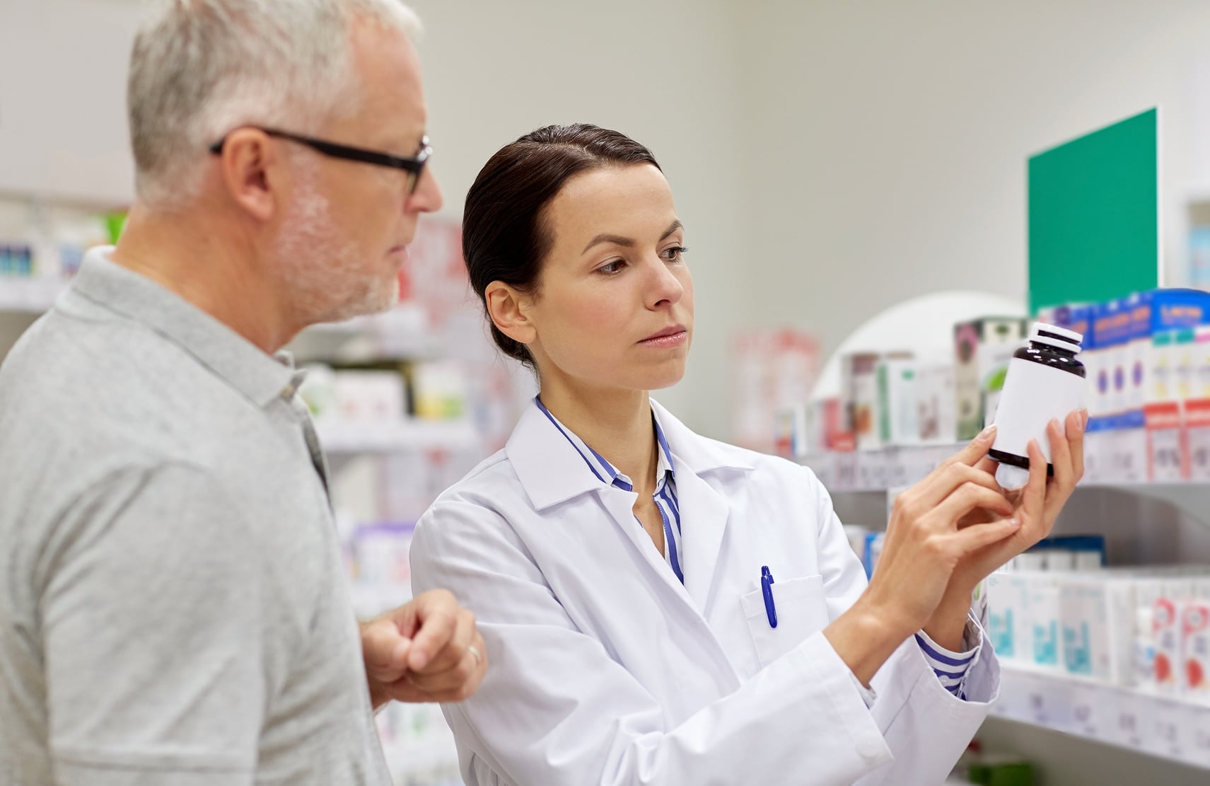 Pharmacist explaining prescription label to older man.