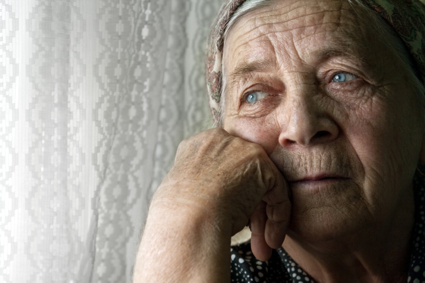 Elderly woman looking sadly out of window.