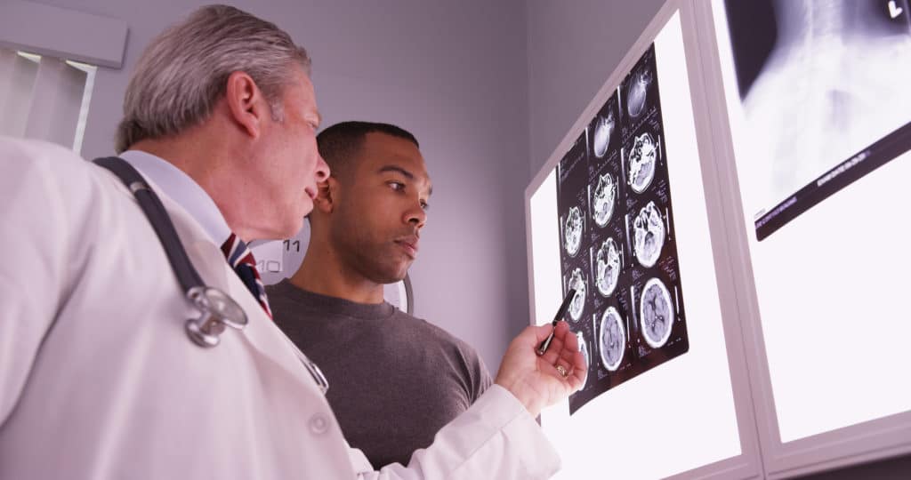 Doctor and young adult man analyzing brain scans.