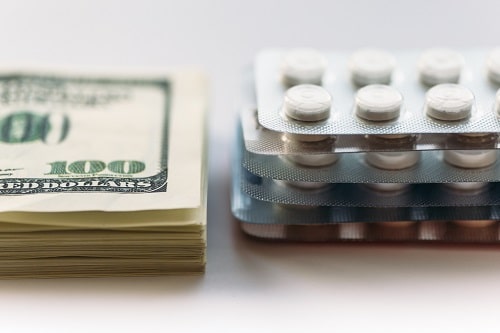 Stack of hundred dollar bills next to stack of pill blister packs.