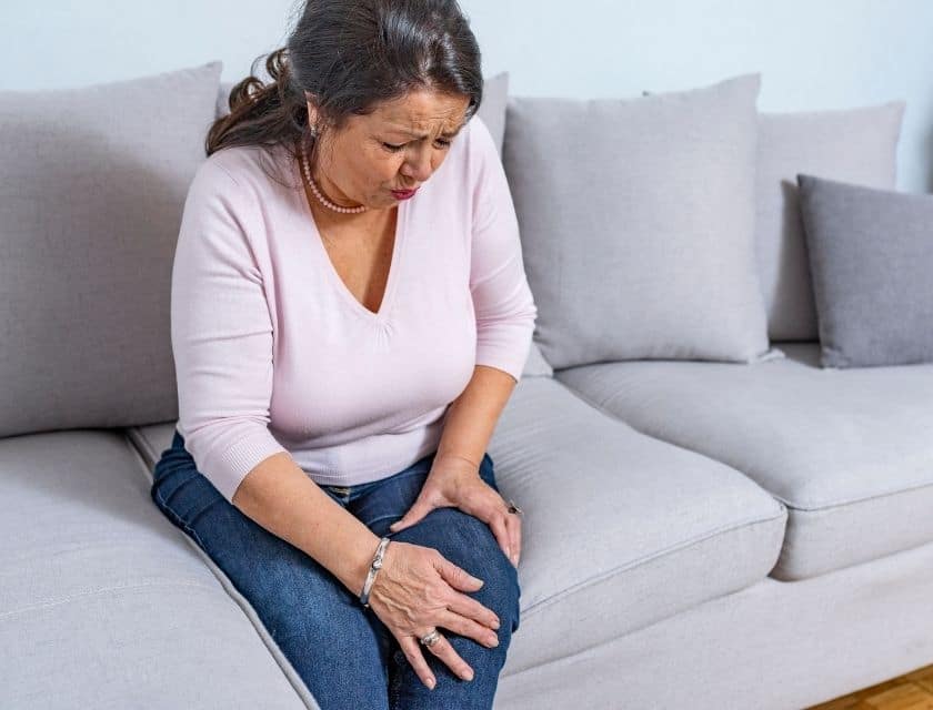 Senior woman sitting on a couch with leg pain.