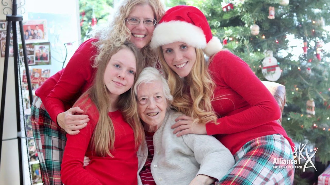 Family in Christmas pajamas hugging grandmother in front of Christmas tree.