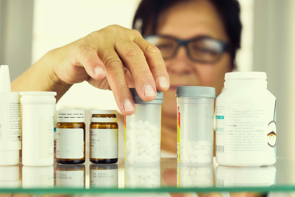 Older woman reading prescription bottles.