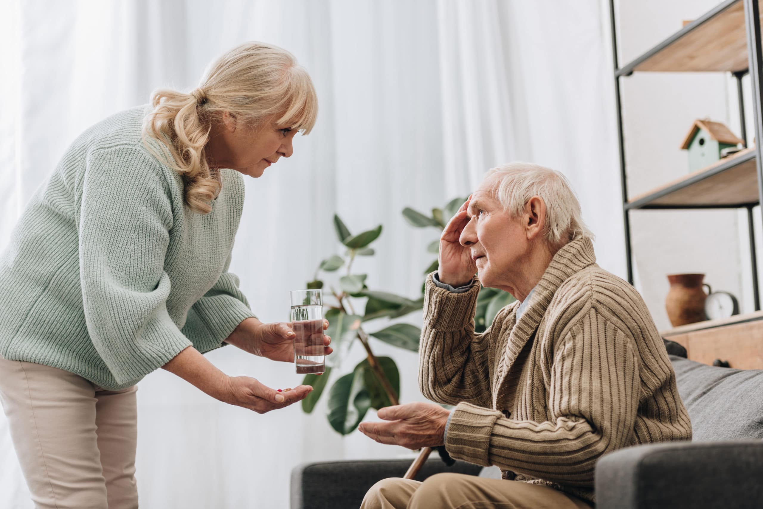 Woman giving medicine to elderly man.