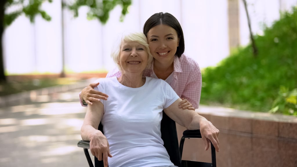 Older woman seated beig hugged from behind by younger woman