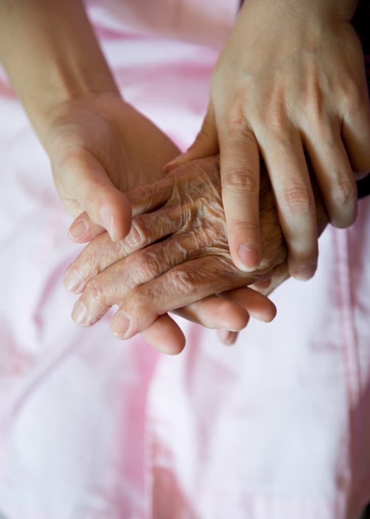 Young hands holding older hand over a bedsheet.