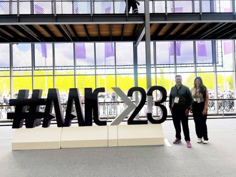 Michael Ward and Adina Lasser stand next to a large #AAIC23 photo station during the conference in Amsterdam in July 2023.