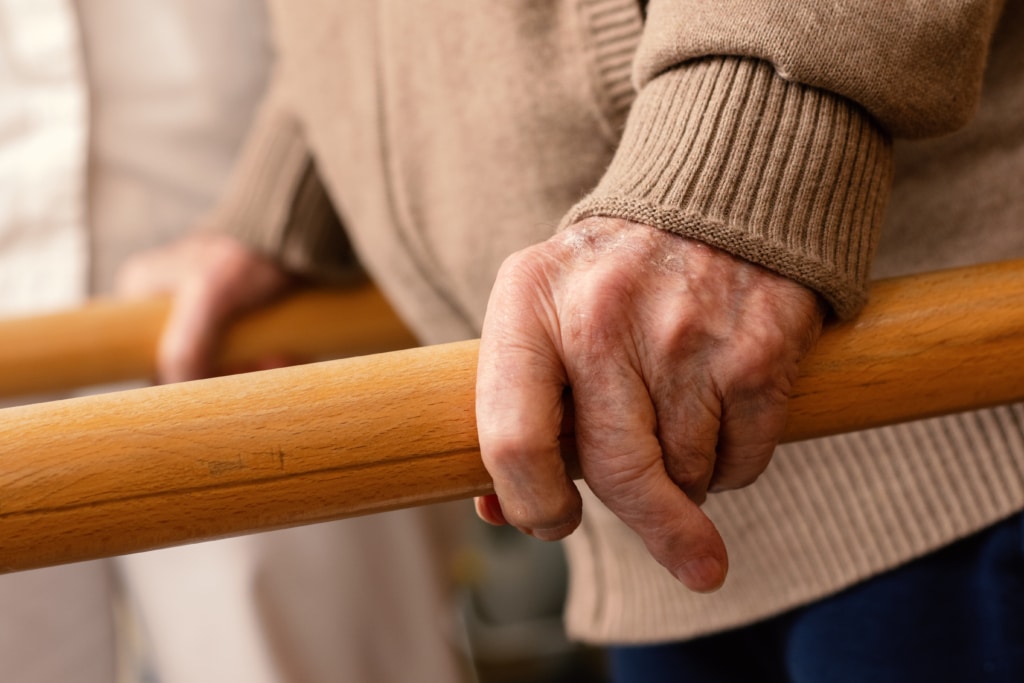 Closeup of older man's hands gripping a rehab stabilization bar.