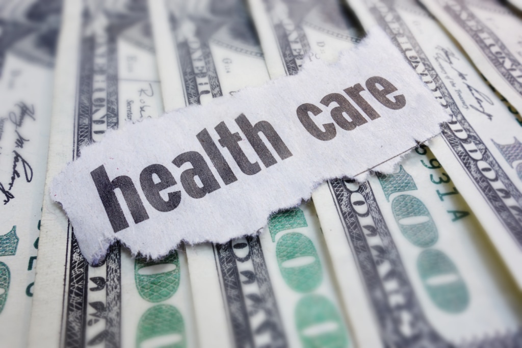 The typed words "health care" laying overtop several $100 bills.
