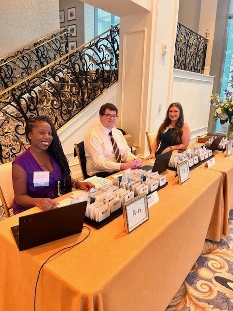 Smiling staff members sitting at a table filled with organized name badges ready to greet guests.