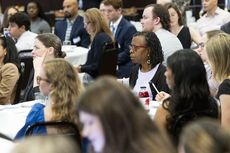 People seated at tables listen to the program.