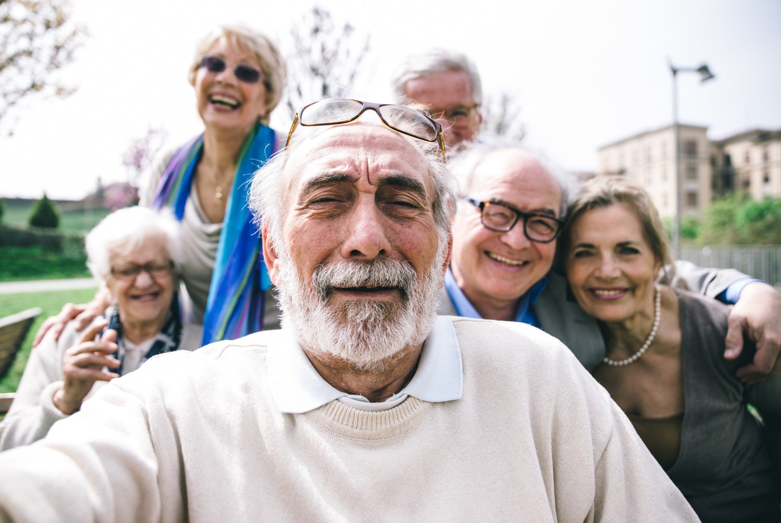 Group of 6 smiling seniors taking a selfie outdoors.