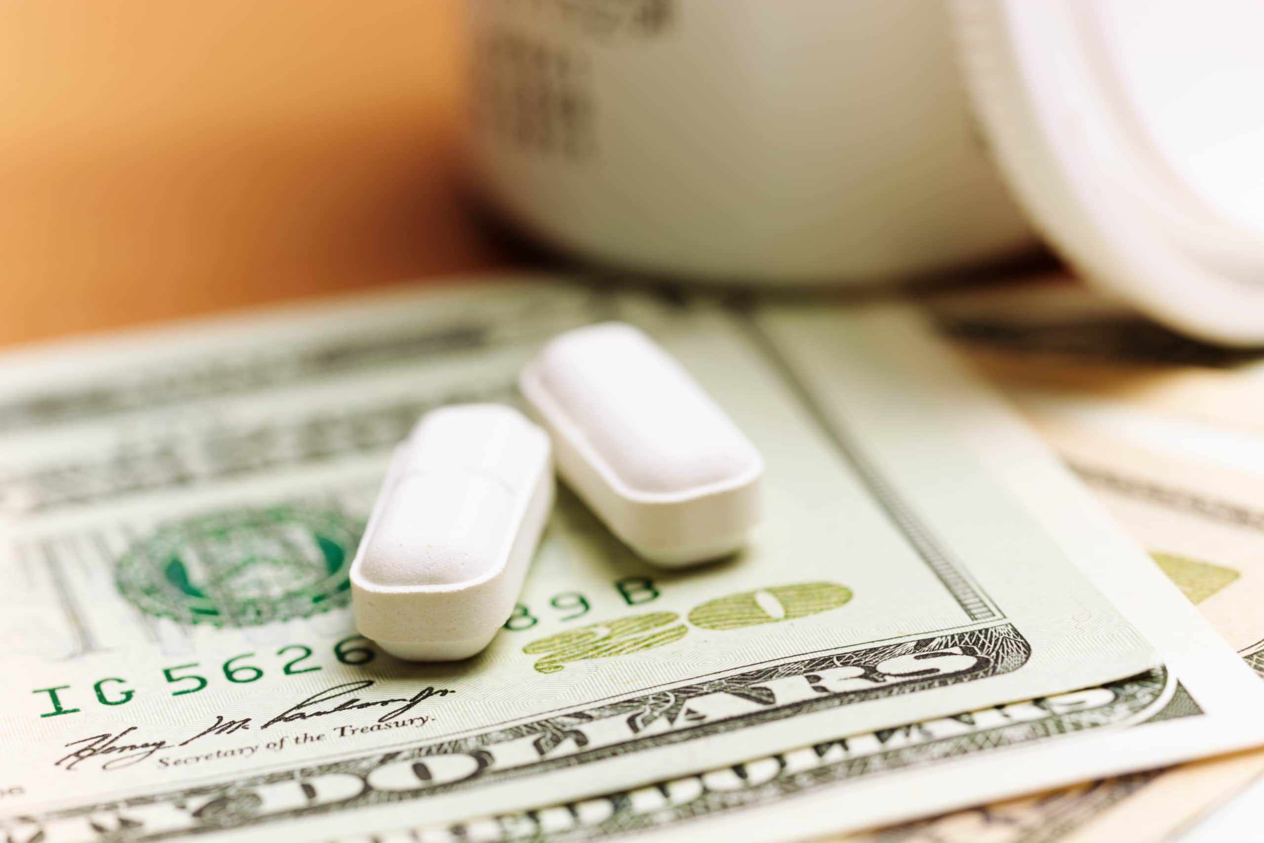 Two oblong white pills sitting on top of some American currency.