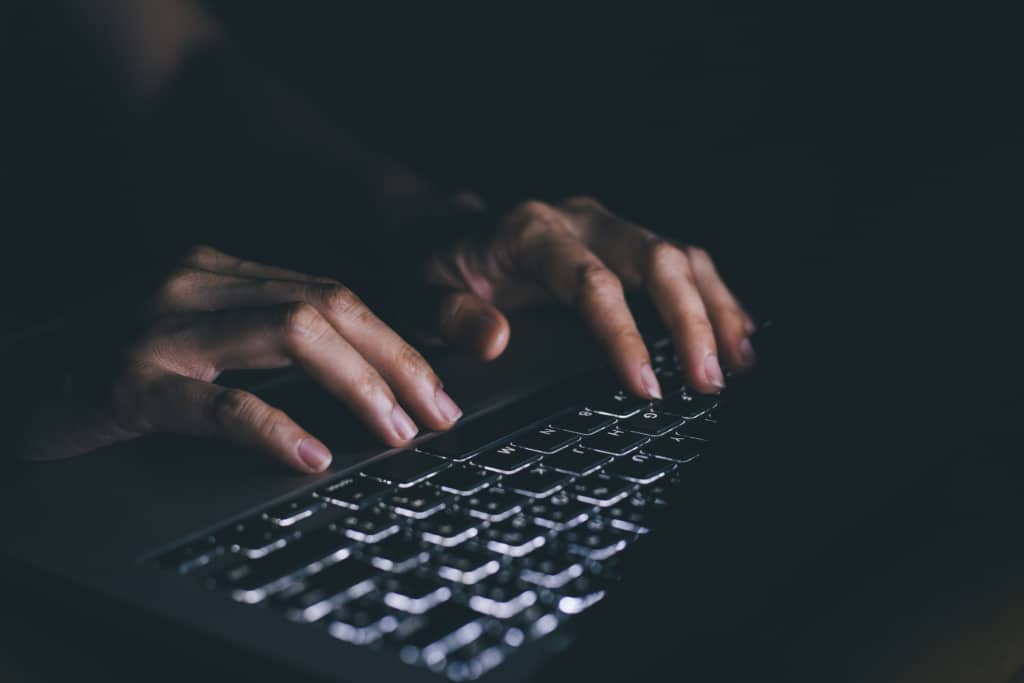 Hands typing on a keyboard in the dark.