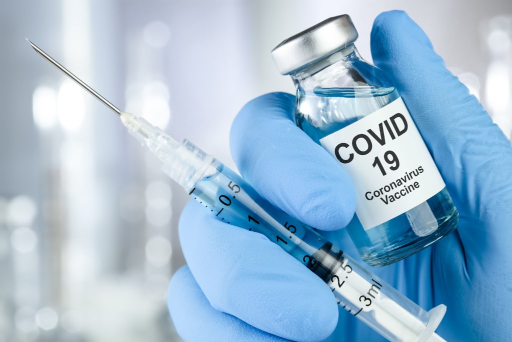 Close-up of a blue gloved hand holding syringe and COVID-19 vial.