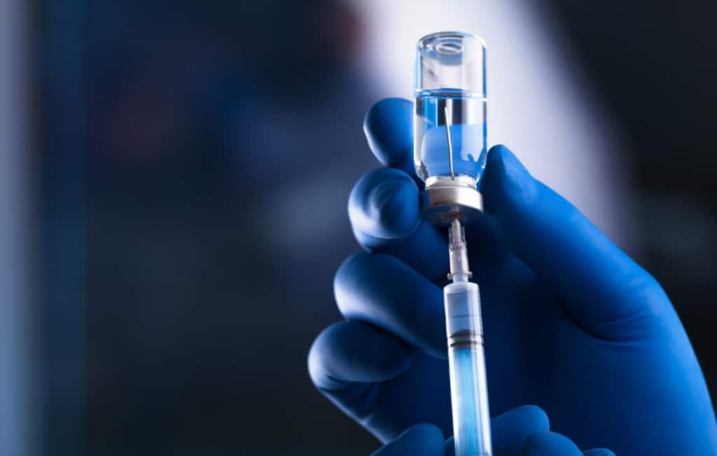 Blue gloved hand holds syringe and vaccine