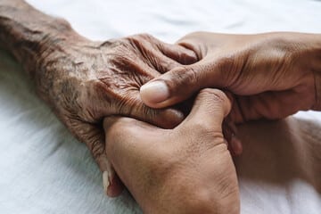 Young hands holding older hands on a white sheet