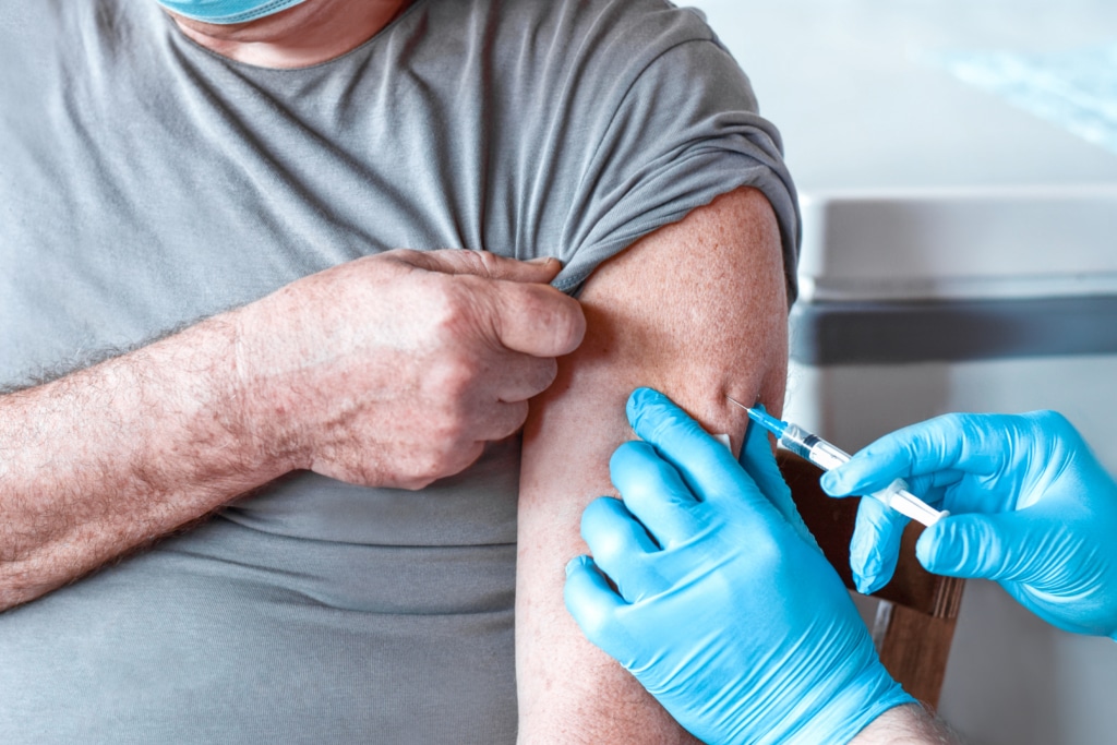 Elderly Man in Face Mask getting Covid Vaccine. Doctor giving Injection to senior Man at Hospital. Virus, COVID-2019 Flu protection. Vaccination of old Patient in Clinic during Coronavirus pandemic.